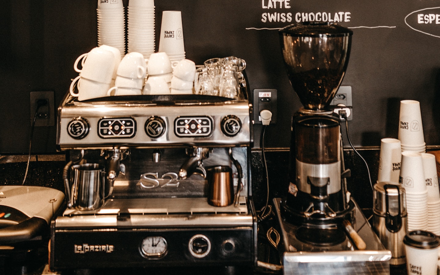A cafe service counter with espresso machine and grinder beneath a menu board
