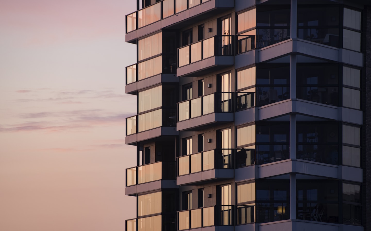 A modern managed residential tower with glass balconies at dusk